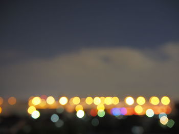 Defocused image of illuminated street lights against sky at night