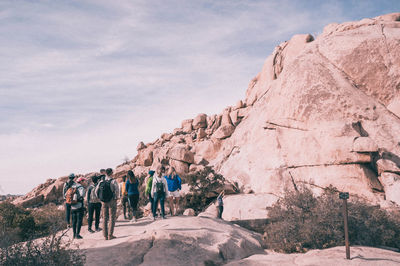 Low angle view of people standing on rock formation against sky