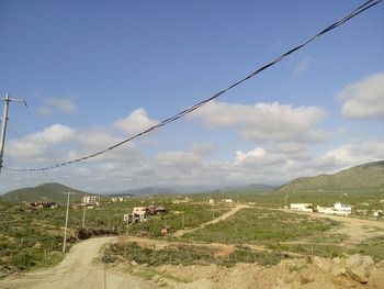 Road passing through field against cloudy sky