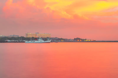 Sea by buildings against orange sky