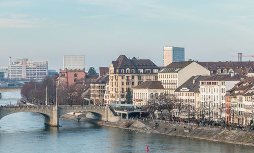 Bridge over river by buildings in city against sky