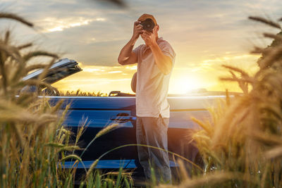 Man photographing while standing on field against sky during sunset