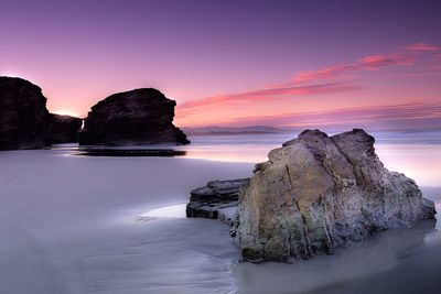 Rock formation in sea against sky during sunset