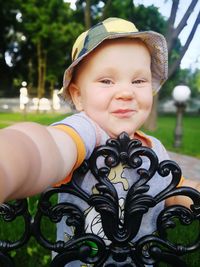 Portrait of cute baby boy standing by railing in park