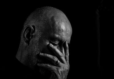 Close-up of depressed man with head in hand against black background