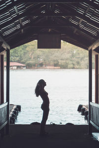 Side view of silhouette woman standing in gazebo against lake