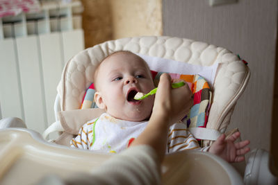 Cropped hand of woman feeding food to baby boy at home
