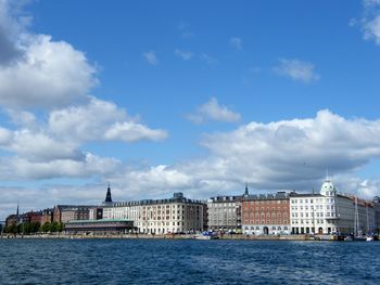 View of buildings by river against cloudy sky