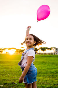 Side view portrait of smiling girl holding balloon while standing at park during sunset