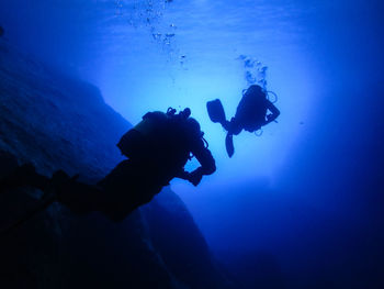 Low angle view of silhouette scuba divers swimming in blue sea