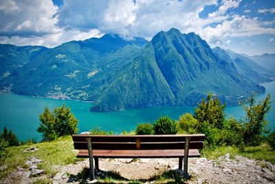 Empty bench by mountains against sky