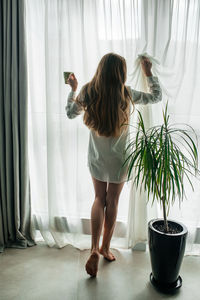 Rear view of woman standing by window at home