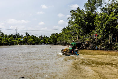 Man riding motorboat in river against sky