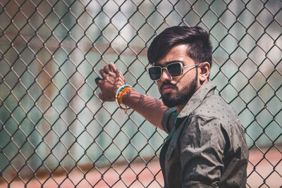 Portrait of young man wearing sunglasses on chainlink fence