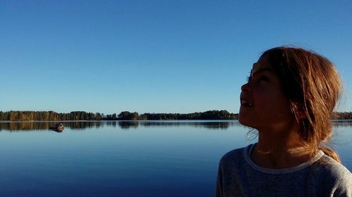 Girl looking away against lake and clear sky