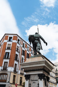 Low angle view of statue by historic building against sky