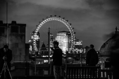 Men standing on bridge against millennium wheel at night