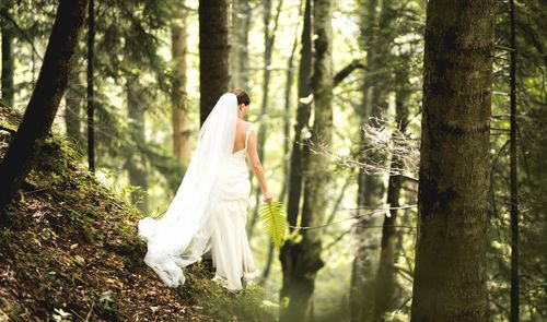 Bride in dress walking by tree at forest