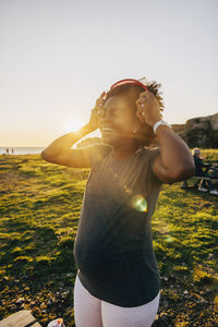 Happy pregnant woman wearing wireless headphones at sunset