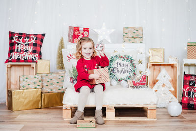 Happy little girl wearing red christmas dress at home over christmas decoration. holding gift box