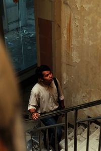Young man looking down while sitting on window