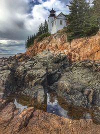 View of lighthouse on cliff against cloudy sky