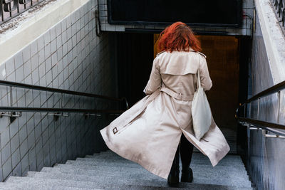 Back view of female walking downstairs in city while entering the city subway