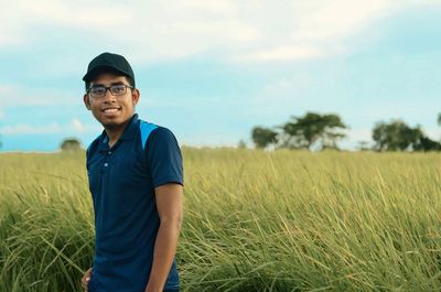 Portrait of young man standing on field against sky