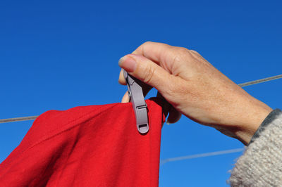 Close-up of hand holding red against blue sky