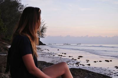 Young woman relaxing on beach against sky