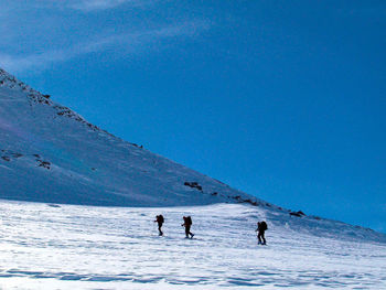 People on snow covered mountain against blue sky