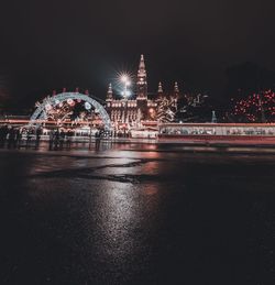 Illuminated city by river against sky at night