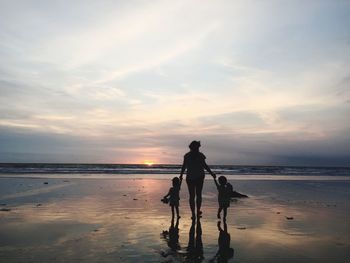 Silhouette people walking on beach against sky during sunset