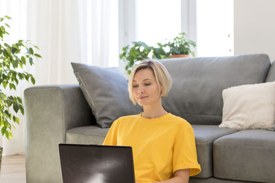 Woman using laptop while sitting on sofa at home