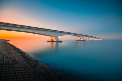 Bridge over sea against blue sky during sunset