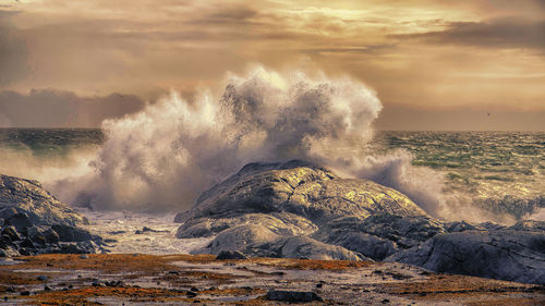 Waves splashing on rocks at shore against sky