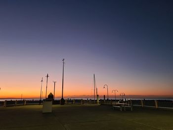 Silhouette street by sea against orange sky