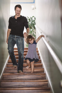 Smiling father holding hands with daughter while climbing steps at home