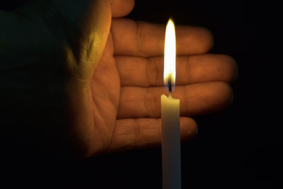 Close-up of hand holding lit candle against black background