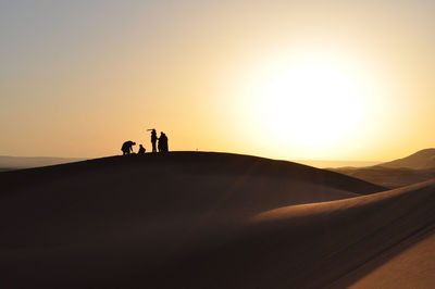 Silhouette people at desert against clear sky during sunset