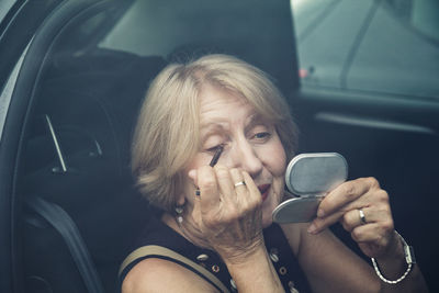 Senior woman applying make up in a car