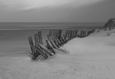 Wooden posts on beach against sky during winter