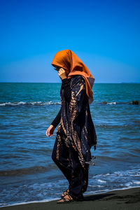 Woman standing at beach against blue sky