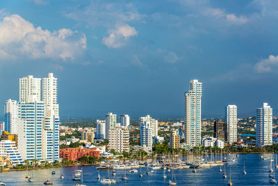 High angle view of boats at harbor by city against cloudy sky