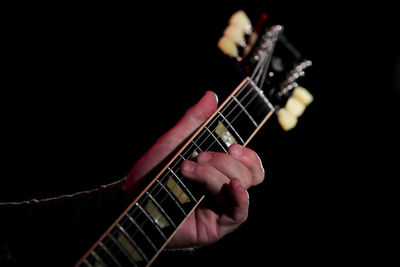 Hand playing guitar against black background