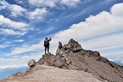 Rear view of hiker standing on rocky mountain against sky