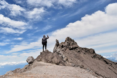 Rear view of man standing on rock against sky