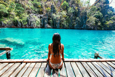 Rear view of woman sitting on pier in sea