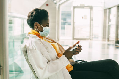 A young african woman in a protective mask sits in a chair in the waiting room 