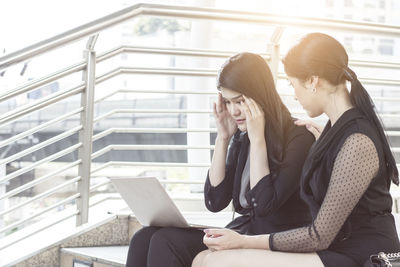 Female colleagues discussing over laptop while sitting on steps against building